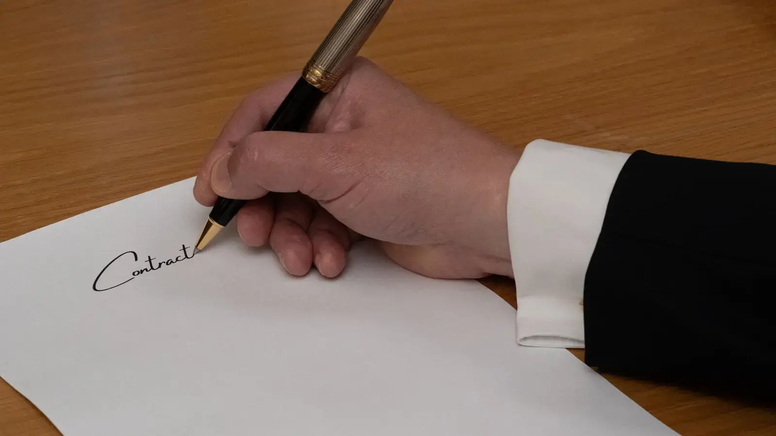 A hand signing a contract with a fountain pen