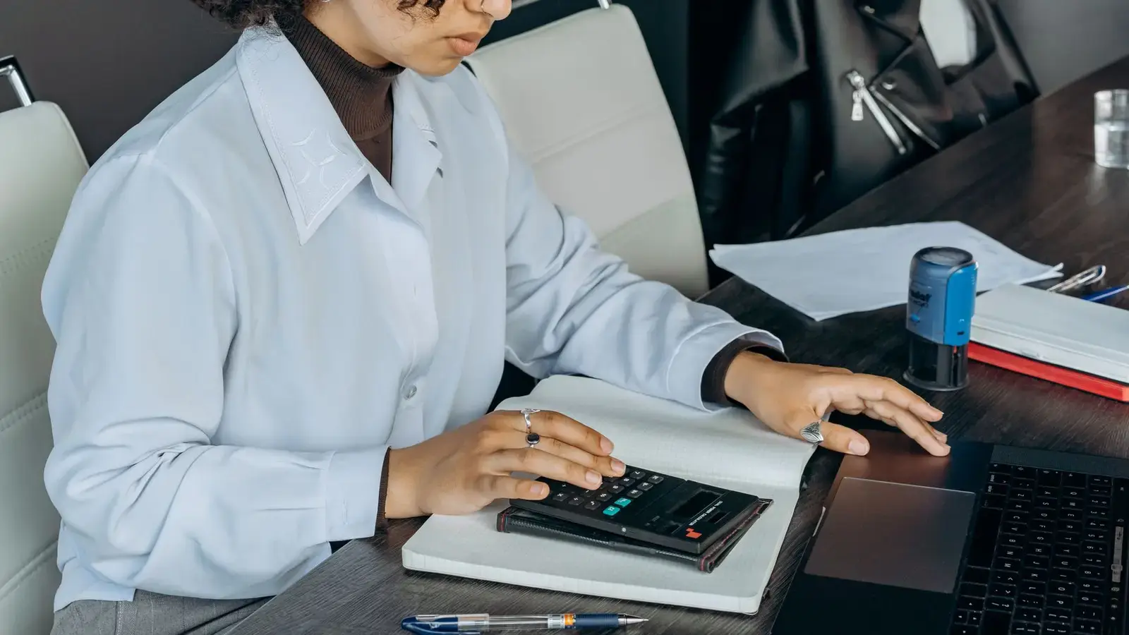 An accountant working with a calculator and a notebook at her desk