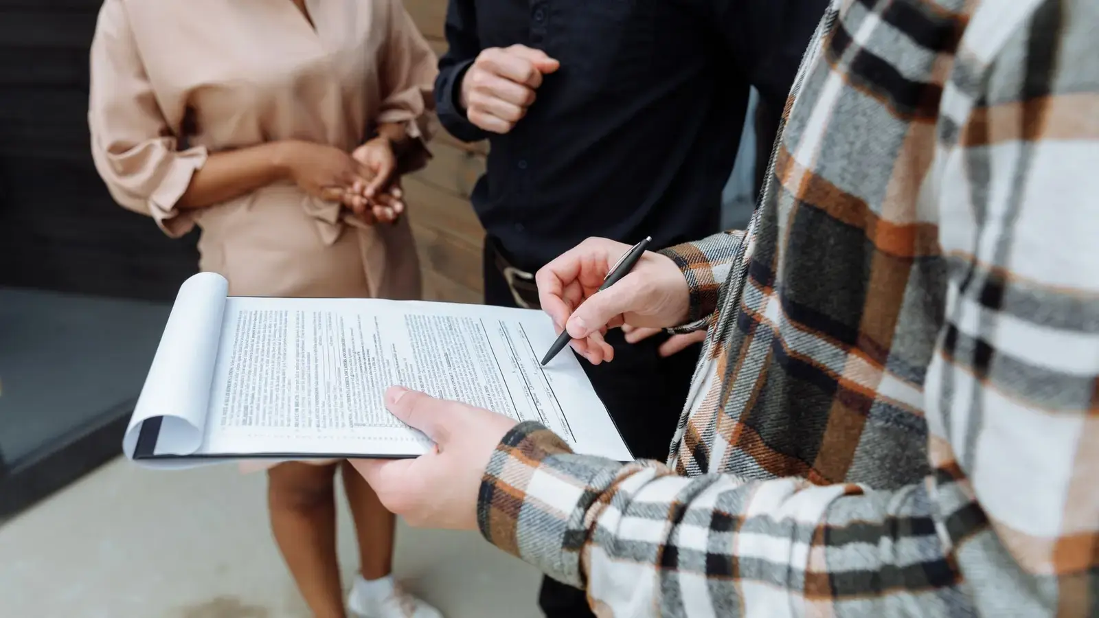 Colleagues standing together as one signs a document on a clipboard
