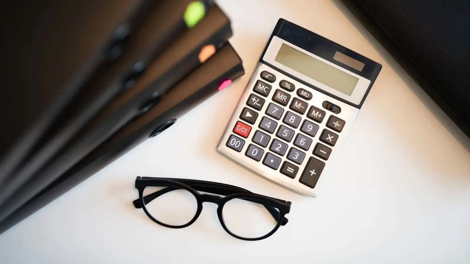 A calculator, glasses and folders on an office desk